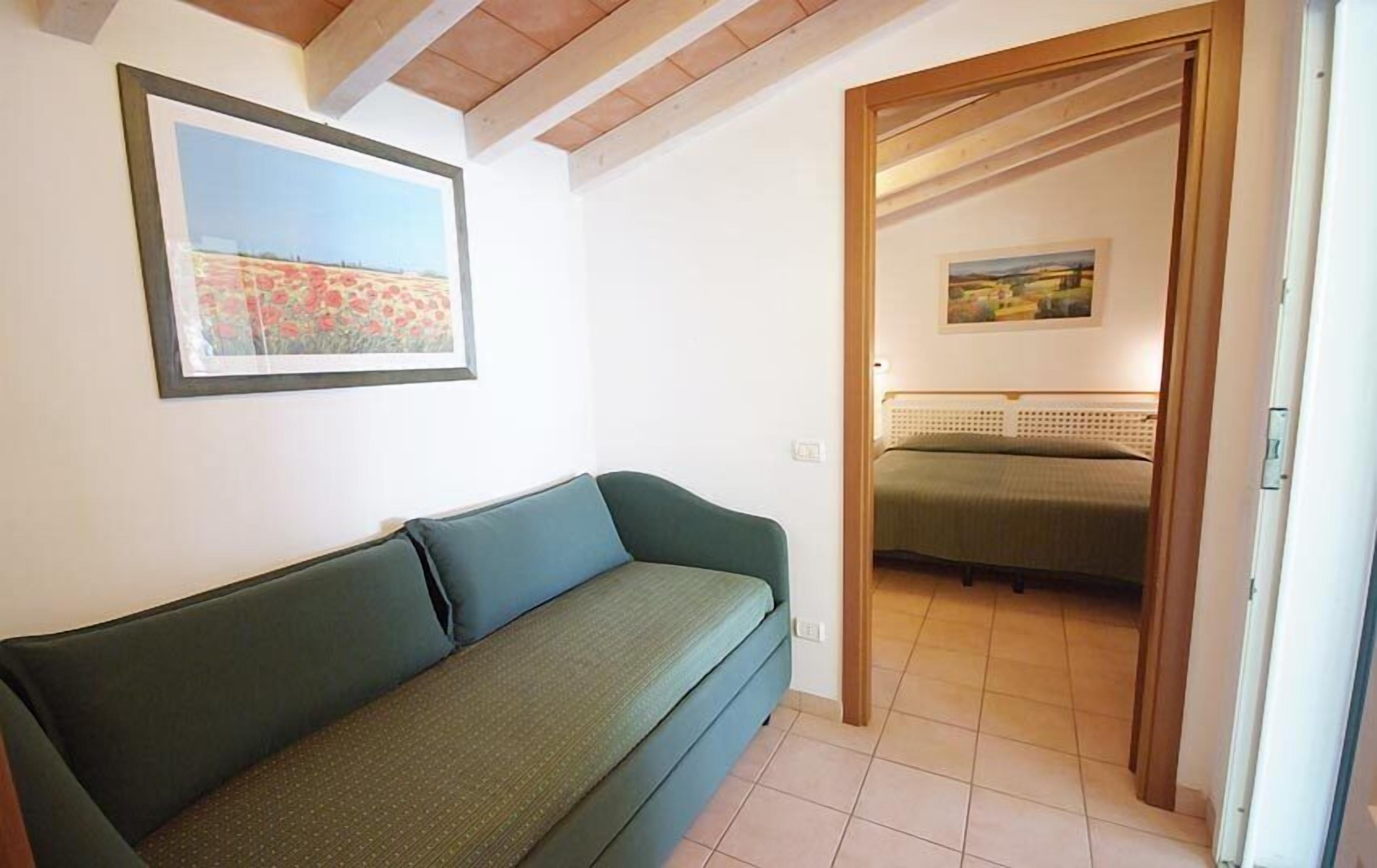 A room with a green sofa, a bed with a green bedspread, and two framed paintings on the walls.