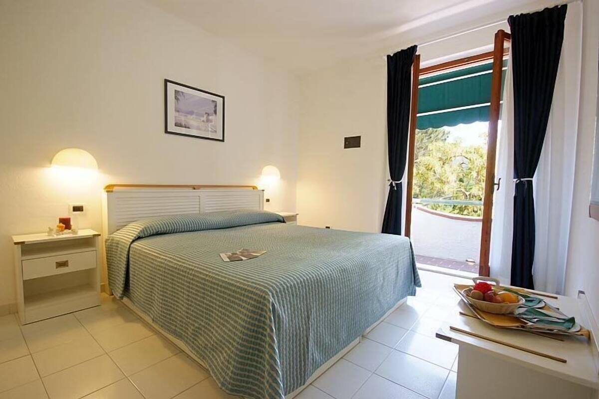 A bedroom with a bed, bedside tables, a window with curtains, and a framed picture on the wall.