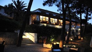A modern house with a stone staircase leading to a balcony, surrounded by trees and outdoor seating. - Hotel Valle Verde (Marciana)