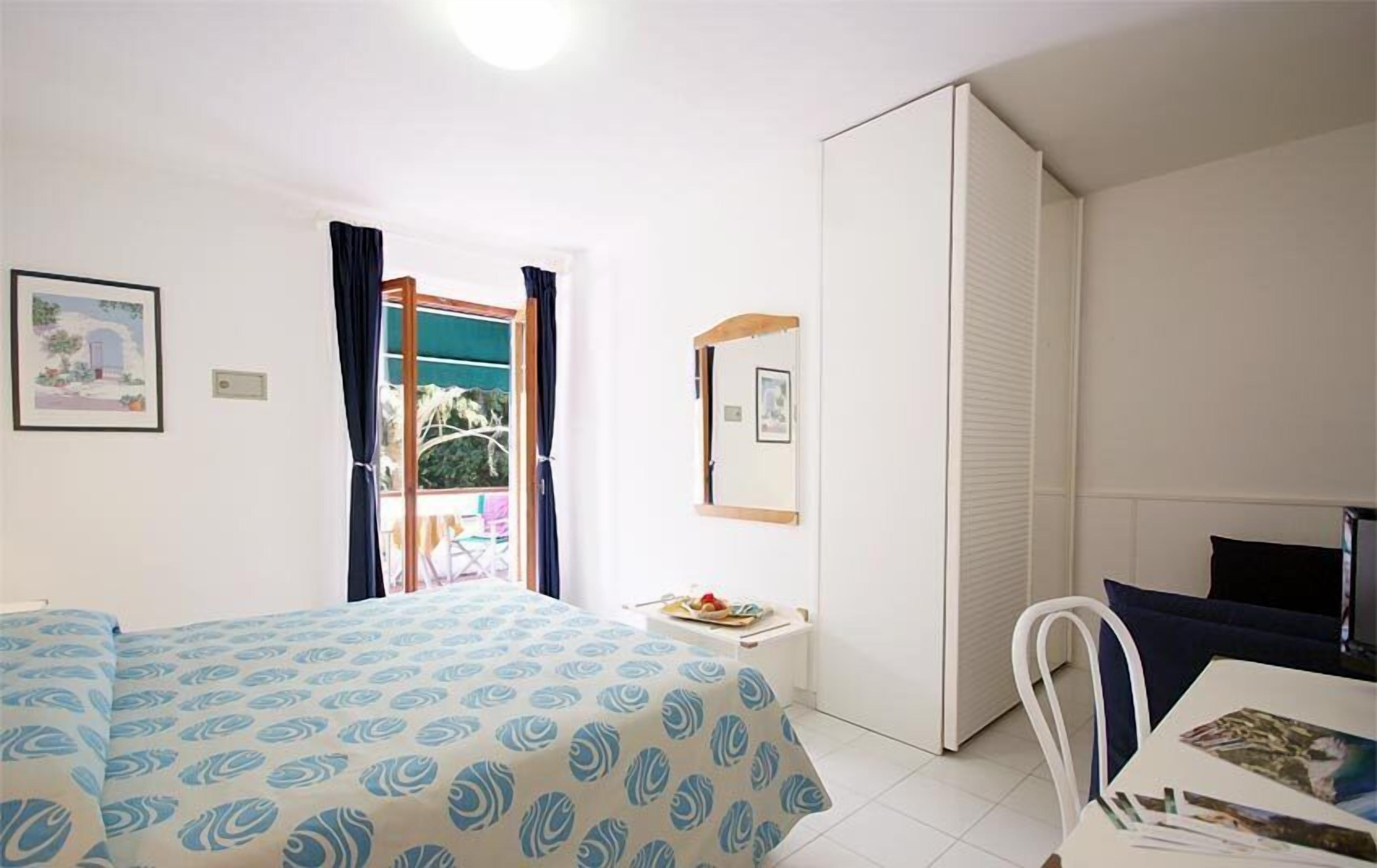 A bedroom with a bed, a desk, a chair, a wardrobe, and a window with curtains.