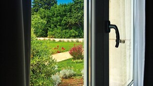 A view through a window with a door handle, revealing a garden with various plants and a pathway. - Beautiful apartment for 6 people with A/C, WIFI, pool, TV and panoramic view (Otranto)