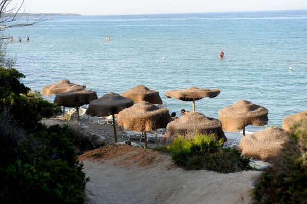 A beach with thatched umbrellas and a sandy area with lounge chairs.