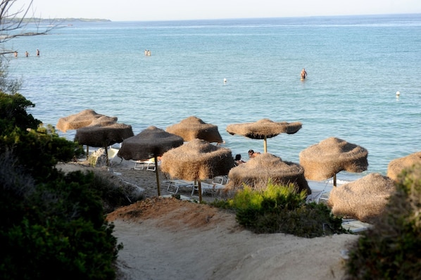 A beach with thatched umbrellas and a sandy area with lounge chairs.