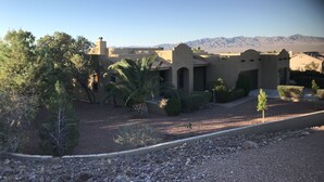 A desert-style building with arched doorways and a flat roof, surrounded by sparse vegetation and a clear view of distant mountains. - Guitar Shaped Pool ! (Bullhead City)