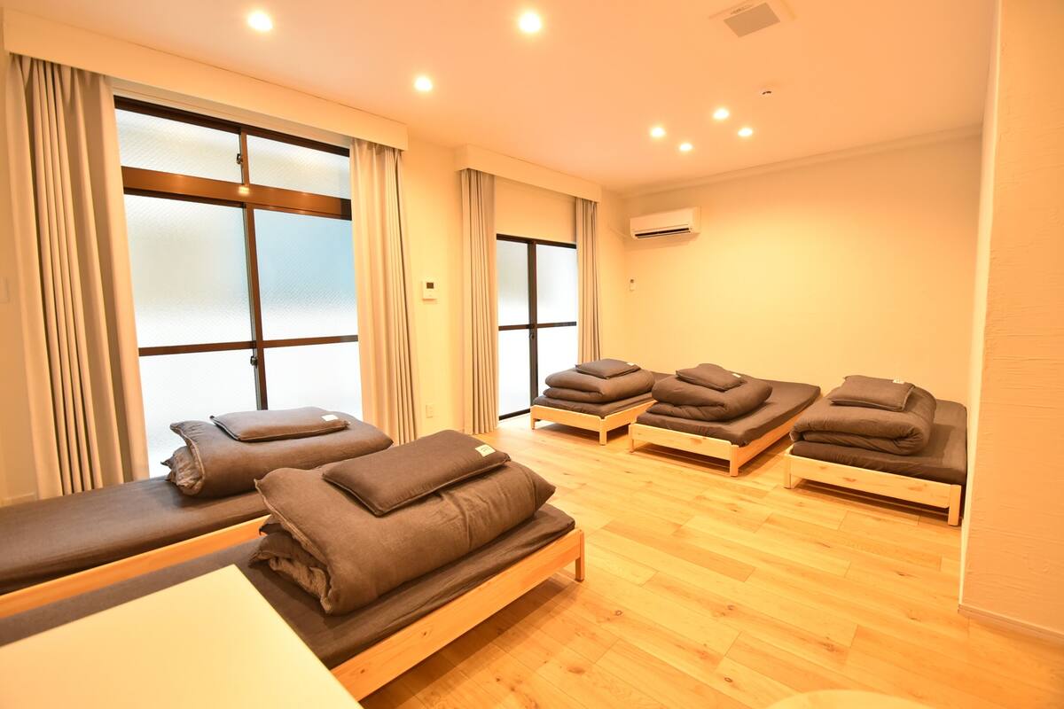 A room with wooden flooring, a massage table, and several massage beds with towels.