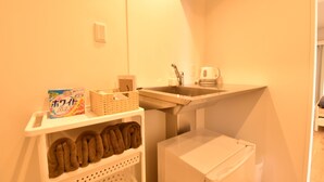 Una cocina compacta con un lavamanos, un hervidor y un estante con toallas y una cesta.