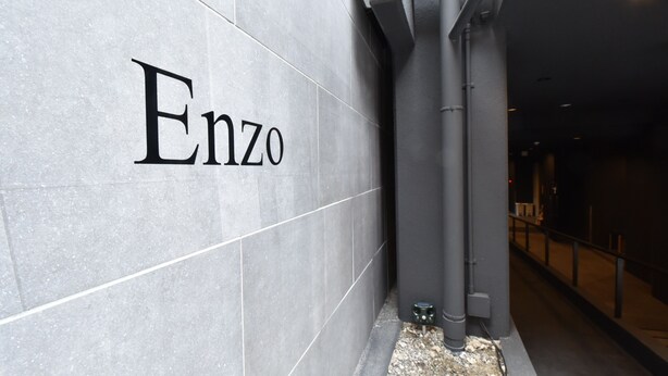Fachada moderna de un edificio con el nombre "Enzo" bien visible en un muro de azulejos.