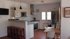 Une cuisine dotée d’un îlot central, de tabourets en bois, d’une table à manger avec des chaises, d’un réfrigérateur et d’une horloge murale.