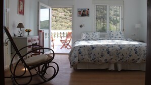 Une chambre à coucher avec un lit, un fauteuil à bascule, un bureau et une vue sur l’extérieur.