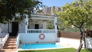Un espace aménagé au bord de la piscine, avec un bâtiment blanc, une bouée de sauvetage et un escalier menant à l’entrée.