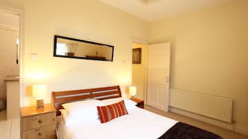 A bedroom with a wooden bed, two bedside tables with lamps, a mirror above the bed, a radiator, and a door to another room.