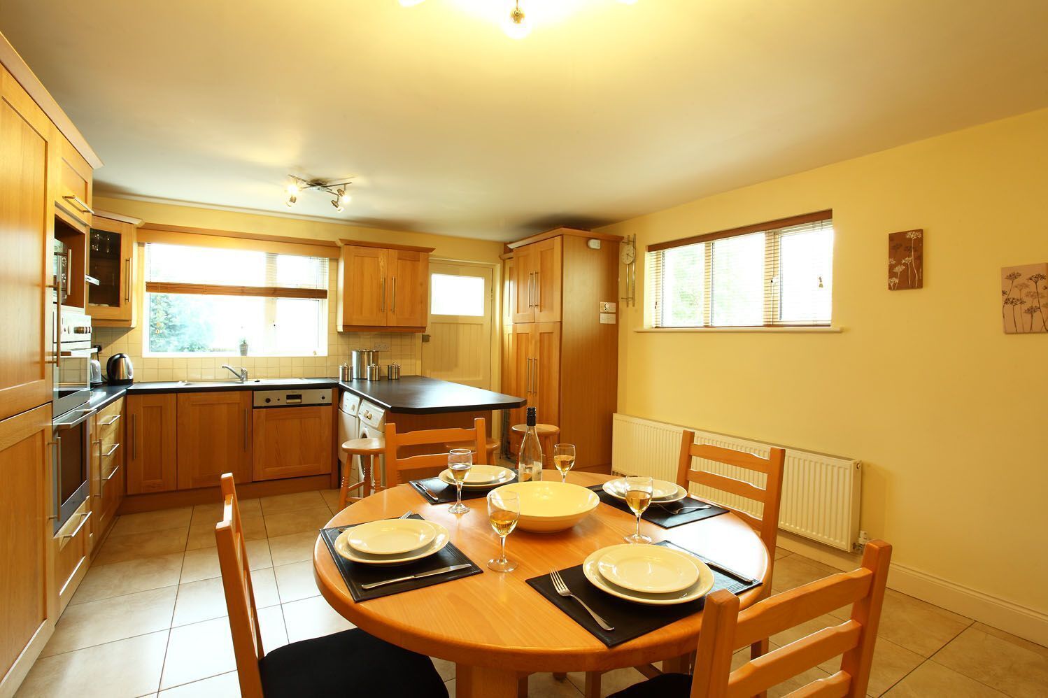 A modern kitchen with wooden cabinets, a black countertop, and a dining area with a round table set for four.