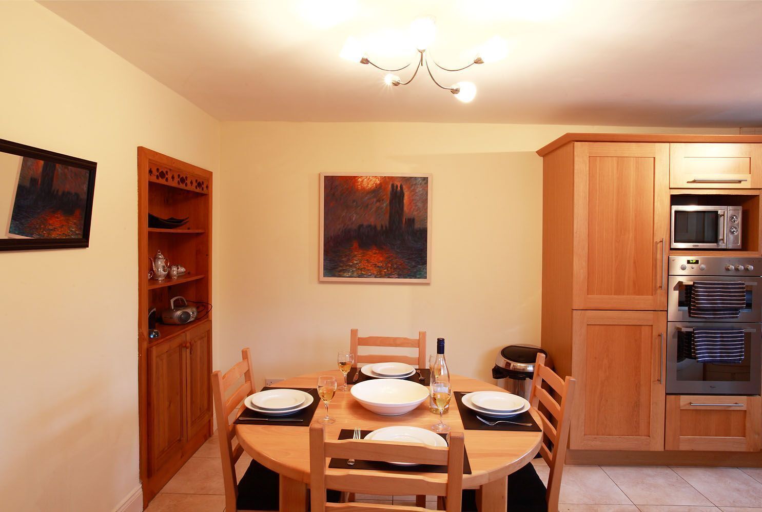 A dining area with a round table, wooden chairs, and a painting on the wall.