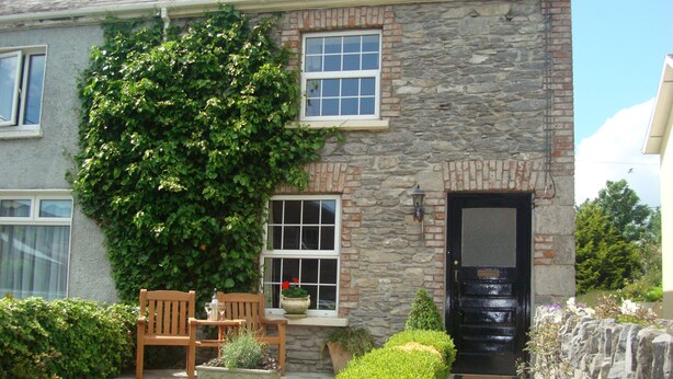 A stone house with a black door, a window with a white frame, and a bench with a potted plant. - Carrig Beag (Kenmare)