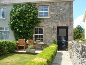 A stone house with a black door, a window with a white frame, and a bench with a potted plant. - Carrig Beag (Kenmare)