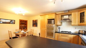 A modern kitchen with wooden cabinets, a large island, a microwave, oven, and a gas stove. - Carrig Beag (Kenmare)