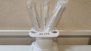 Valkoinen teline, jossa on sana ”OLIVE”, ja jossa on useita tuotteita, joiden etiketissä lukee ”TOOTH BRUSH”.
