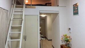 Opiskelija-asuntotyylinen huone, jossa on kerrossänky, tikkaat, pieni keittiö ja käytävä, joka johtaa kylpyhuoneeseen.