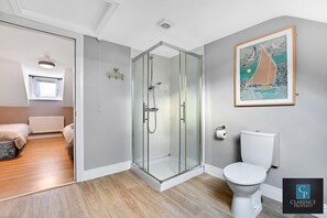 A modern bathroom with a glass shower enclosure, a toilet, and a framed artwork on the wall. - Hestia House  (Londonderry)
