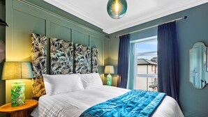 Ein Schlafzimmer mit einem großen Bett, zwei Nachttischen, einer grünen Wand, einem Fenster mit Vorhängen und Blick auf Gebäude.