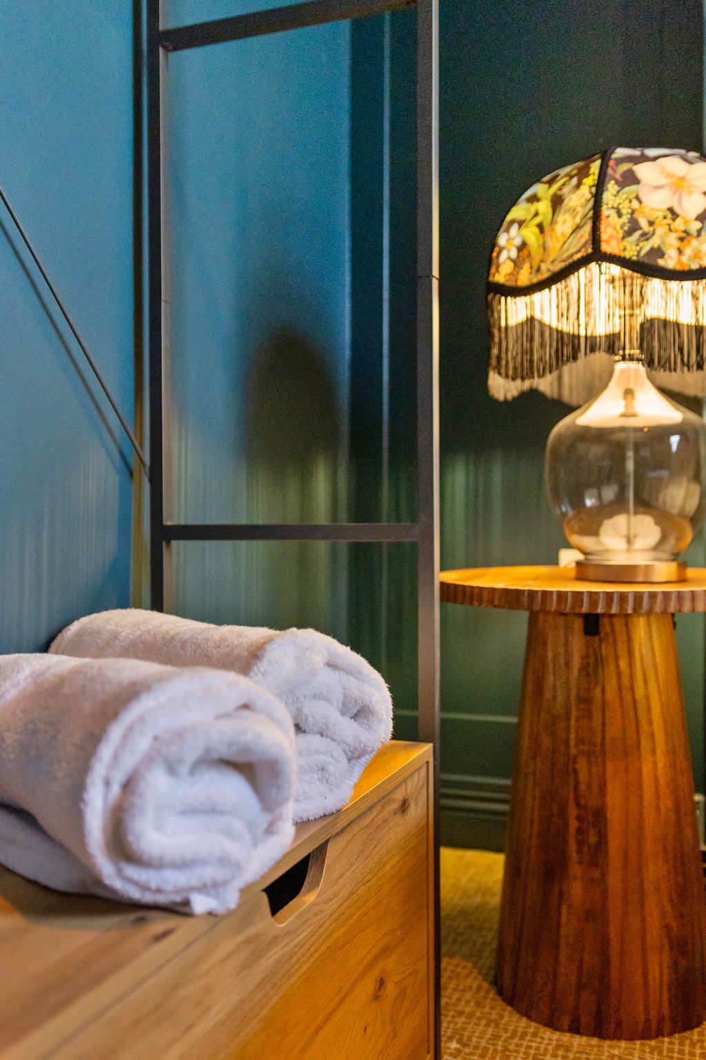 A wooden chest with folded towels, a lamp with a floral shade, and a blue wall.