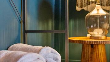 A wooden chest with folded towels, a lamp with a floral shade, and a blue wall.
