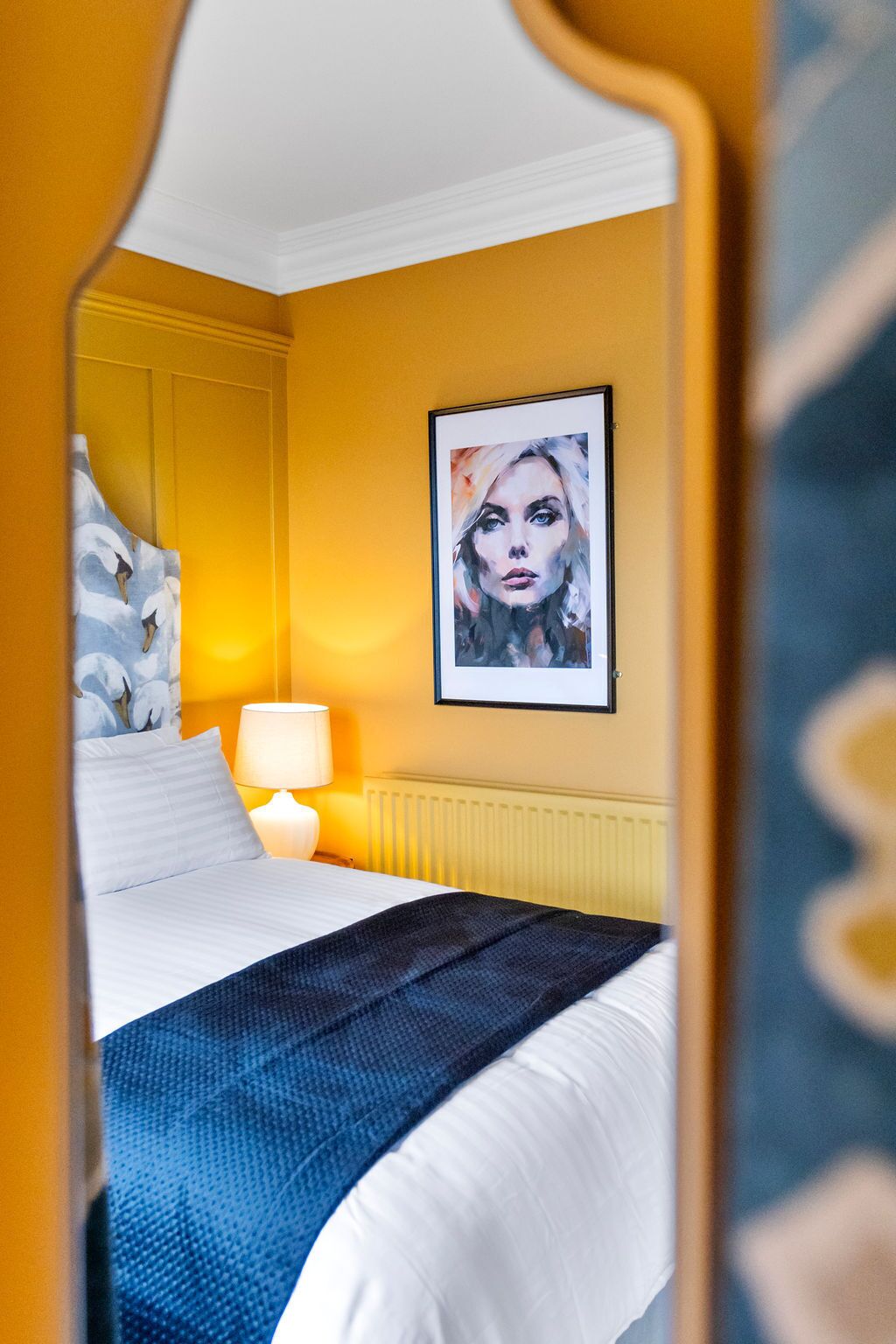 A hotel room with a bed, a nightstand, a lamp, and a framed artwork on the wall.