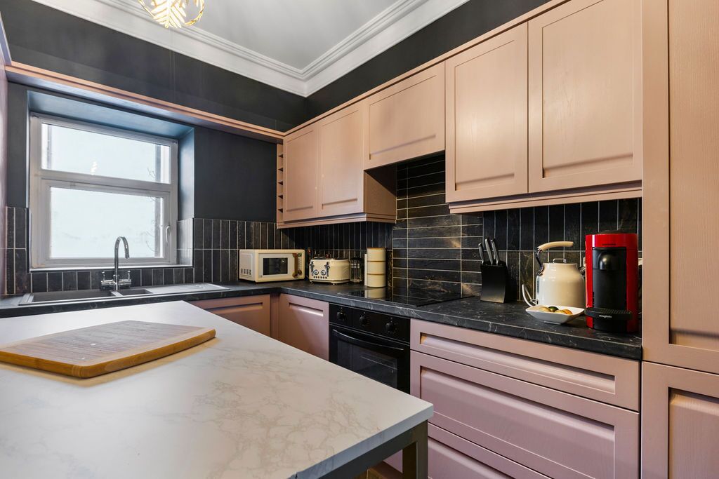 A kitchen with light wood cabinets, a black countertop, a microwave, a coffee maker, and a window providing natural light.