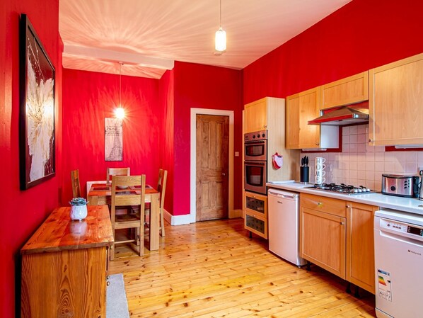 A compact kitchen with wooden cabinets, a dining table with chairs, and a red wall.