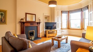A living room with a fireplace, a television, and comfortable seating. - Beautiful and Bright Georgian Style Morningside Apartment - Pass the Keys (Edinburgh)