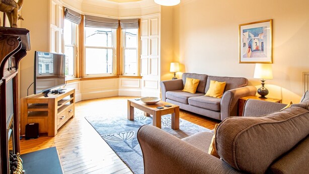 A living room with a fireplace, a television, a sofa, and a painting on the wall. - Beautiful and Bright Georgian Style Morningside Apartment - Pass the Keys (Edinburgh)