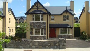 A two-story house with a stone facade, a red door, and a stone wall in front. - Ardmullen 4 bed Walnut (Kenmare)