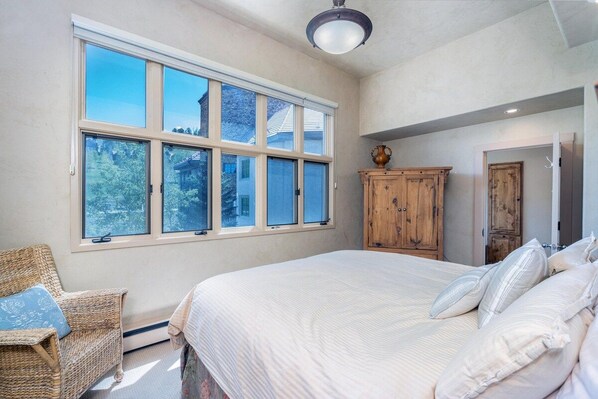 Een slaapkamer met een groot bed, een rieten stoel en een houten kast.