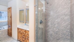 Een badkamer met een douchecabine van glas, een houten wastafelmeubel met spiegel en een bad.