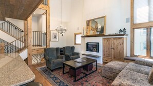 Een ruime woonkamer met een open haard, een trap en een groot raam.