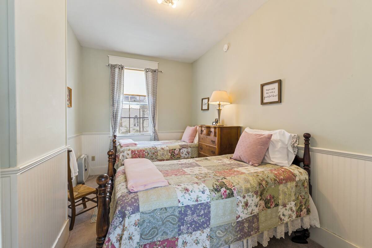 A bedroom with two beds, a dresser, a lamp, and a window with curtains.