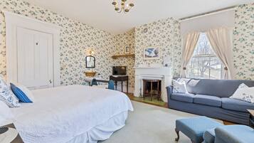 A bedroom with a large bed, a sofa, a fireplace, and floral wallpaper.