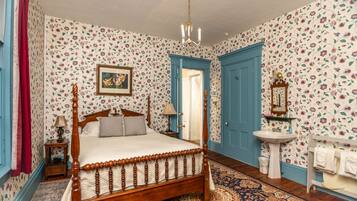 Une chambre à coucher avec un lit à baldaquin en bois, un papier peint à motifs floraux, un lustre, une table de chevet avec une lampe et une commode.