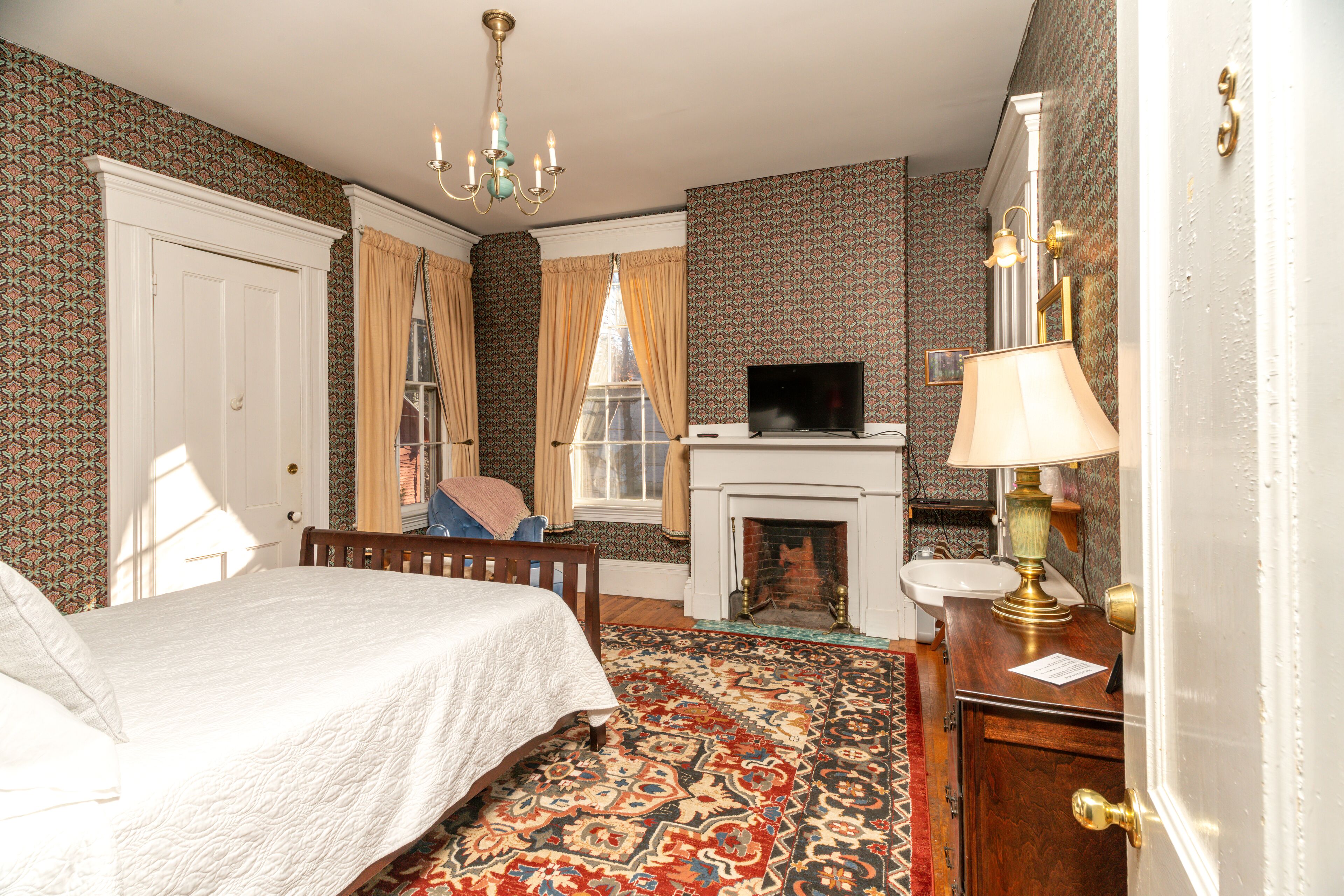 A bedroom with a bed, a television, a fireplace, and patterned wallpaper.
