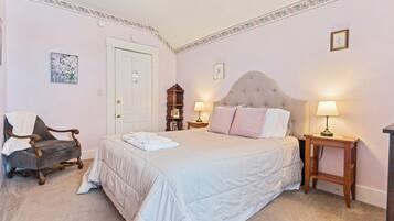 A bedroom with a large bed, two bedside tables with lamps, a chair, and a door.
