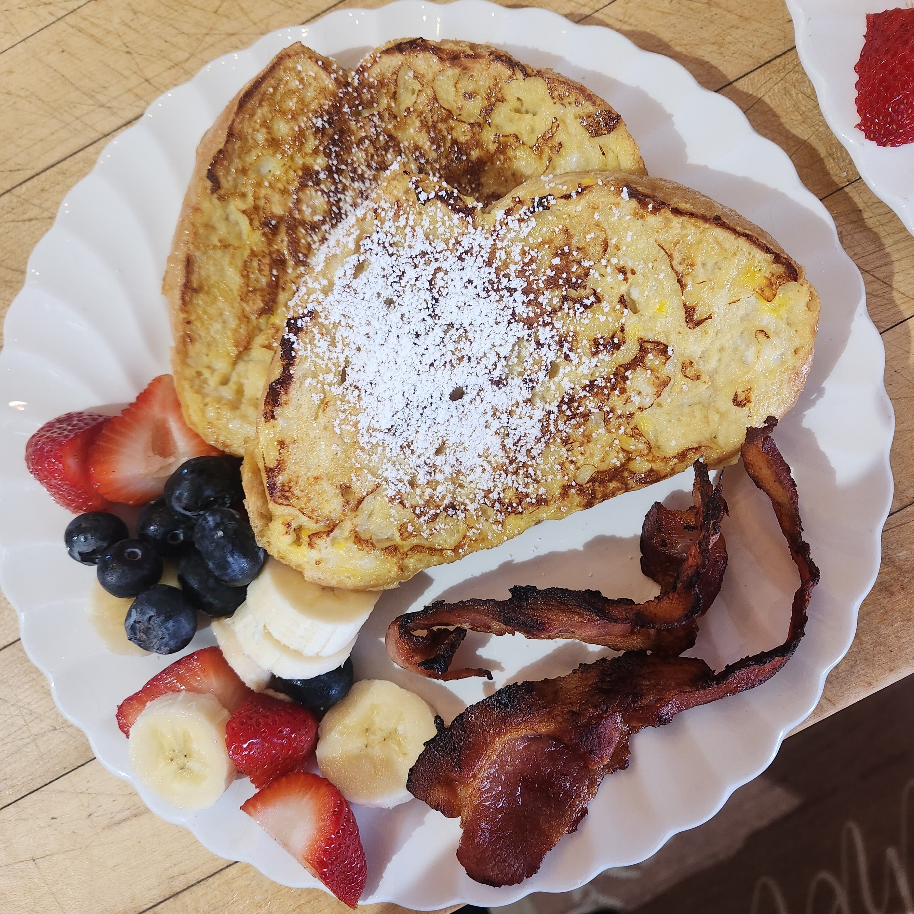 A plate with French toast, strawberries, blueberries, banana slices, and bacon.