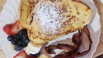 A plate with French toast, strawberries, blueberries, banana slices, and bacon.