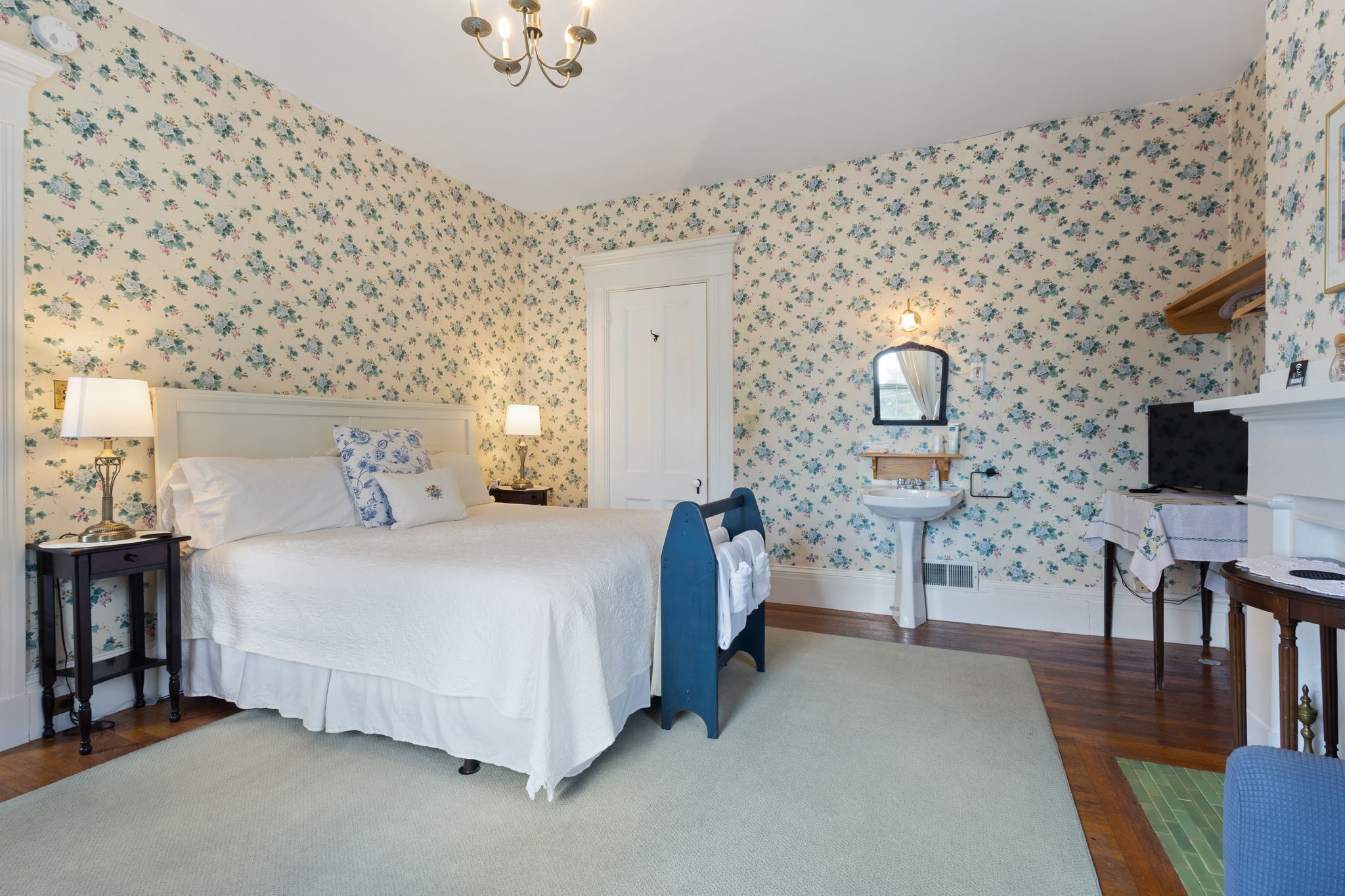 A bedroom with a bed, bedside tables, a nightstand, a dresser, a mirror, and a desk with a chair.