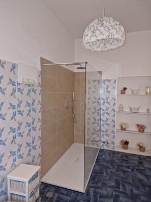 A shower area with a glass door, tiled walls with a leaf pattern, and a patterned ceiling light. - Villa Oliveta (San Gimignano)
