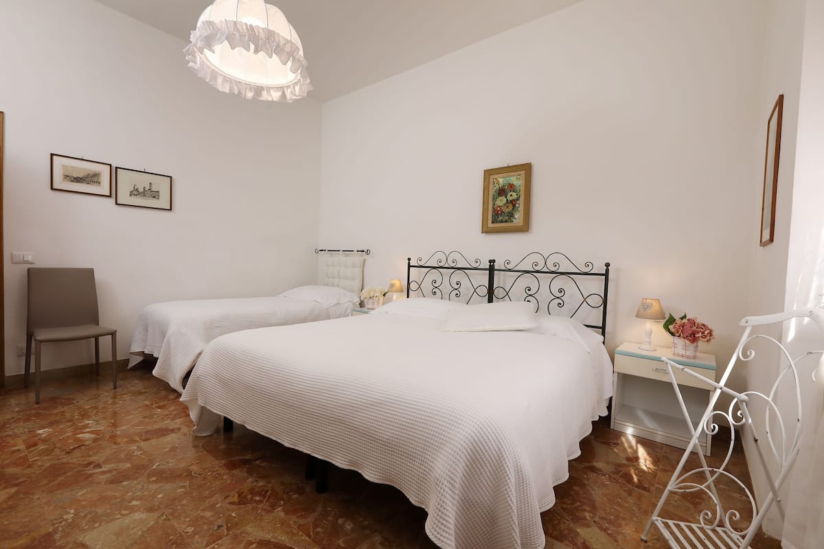 A bedroom with two beds, a chair, a small table with a lamp, and a picture on the wall.