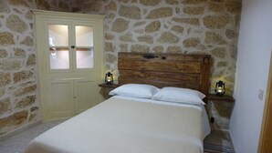 A bedroom with a stone wall, a wooden headboard, a bed with white linens, and two nightstands with lanterns.