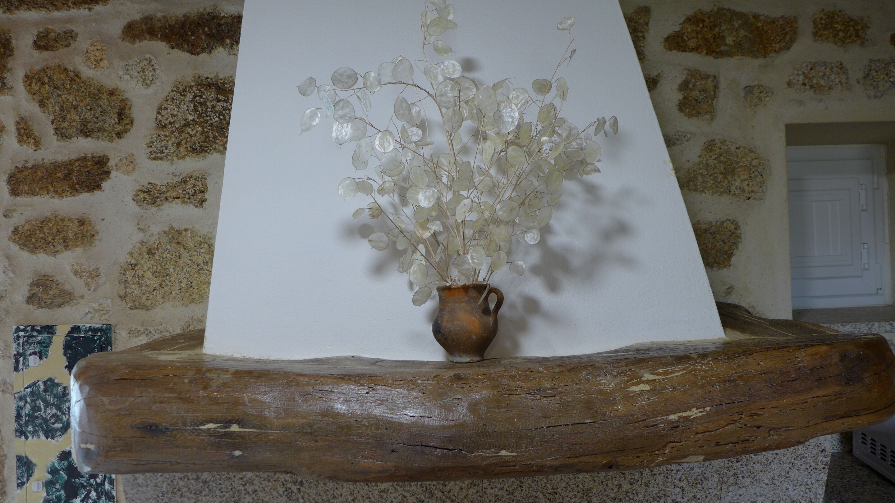 A rustic wooden shelf holding a vase with white flowers against a stone wall.