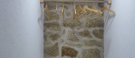 Une petite pièce étroite avec un mur en pierre, un plafond en bois et un lit recouvert de draps blancs.