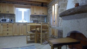 A rustic kitchen with wooden cabinets, a stone wall, and a fireplace.