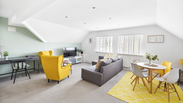 A modern living room with a sofa, yellow chairs, a dining table, and a TV. - 84A Albany Road (Cardiff)